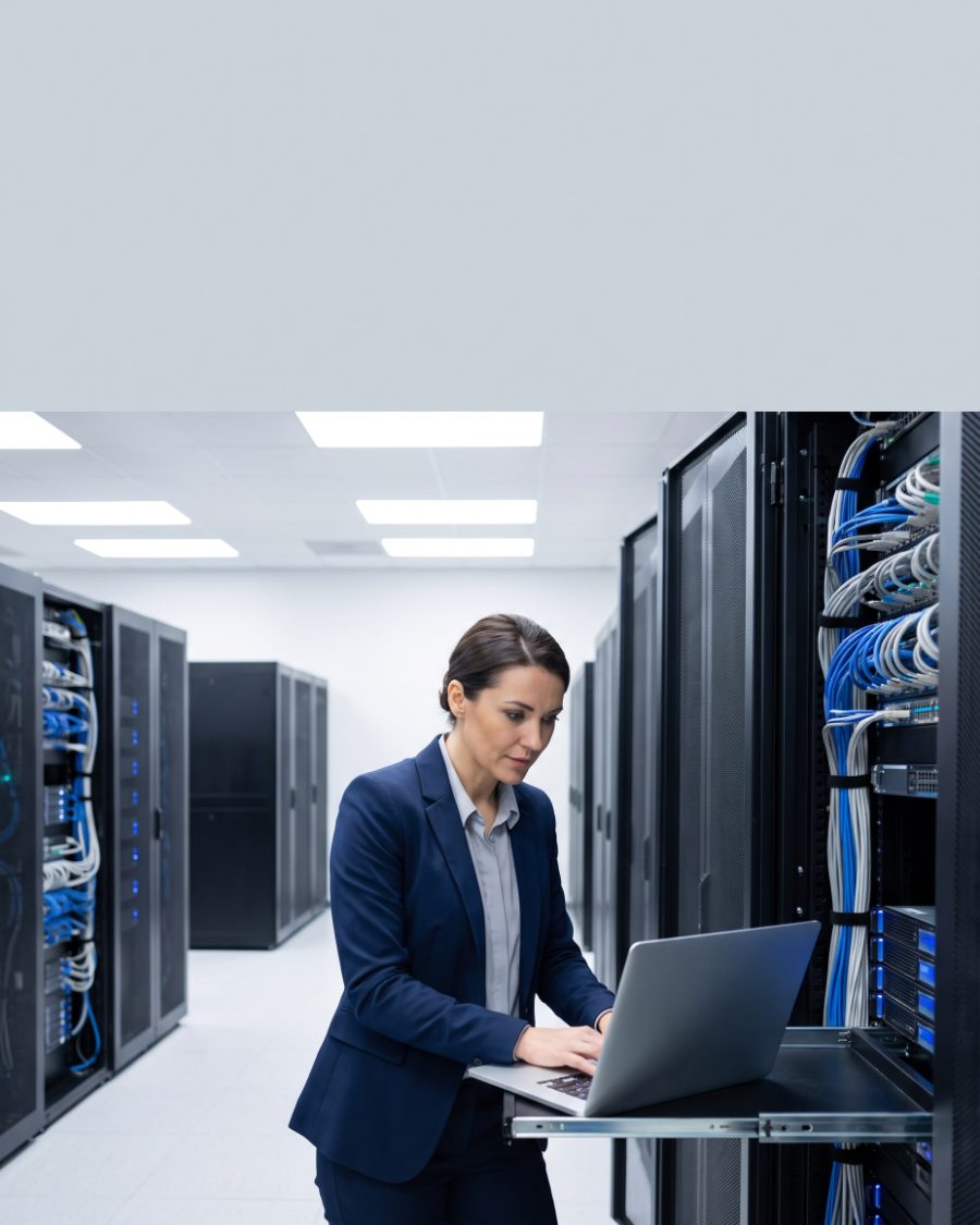 Technician working on a laptop beside server racks in a clean data center aisle